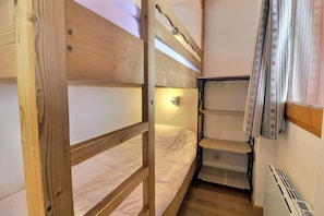 A compact room with a bunk bed, a small shelf unit, and a radiator.