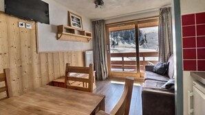 A cozy room with a wooden dining table, chairs, a sofa, and a large window with a view of a snowy landscape. - 10m from ski slopes, 5th floor, balcony, ski locker, 20m², Méribel-Mottaret (Méribel - Les Allues)