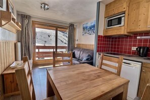 A cozy kitchen with wooden furniture, a dining table, a sofa, and a view of a snowy landscape through a large window.