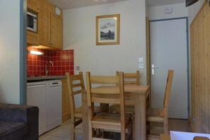 Una cocina compacta con armarios de madera, salpicadero de azulejos rojos y una mesa de comedor con sillas.