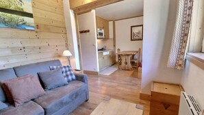 A cozy living room with a sofa, a wooden floor, and a kitchen area in the background. - 10m from ski slopes, 3rd floor, balcony, ski locker, 21m², Méribel-Mottaret (Méribel - Les Allues)