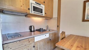 A compact kitchen with wooden cabinets, a built-in microwave, a kettle, and a sink. - 10m from ski slopes, 3rd floor, balcony, ski locker, 21m², Méribel-Mottaret (Méribel - Les Allues)