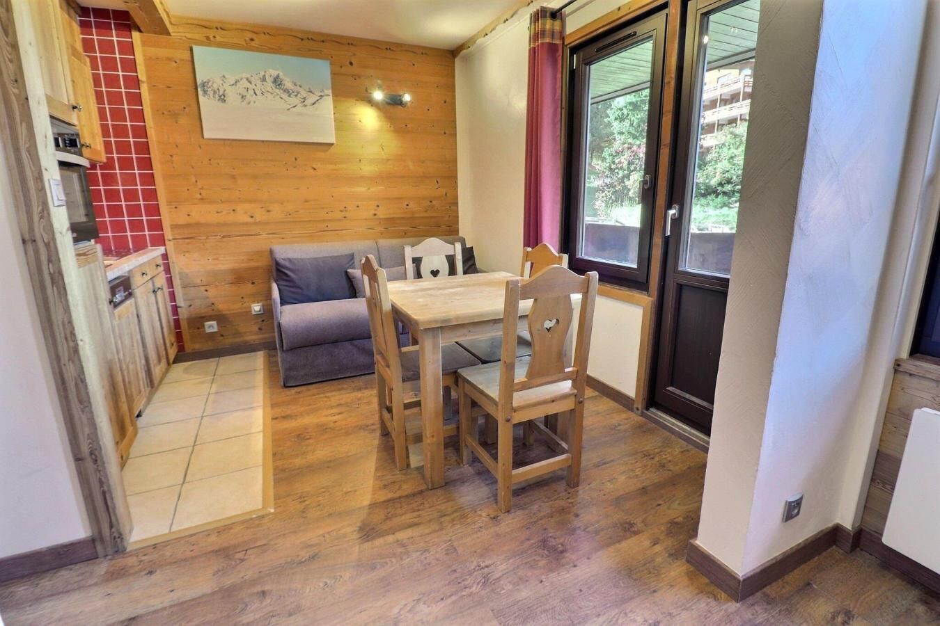 Eine kompakte Küche mit Holzausstattung, einem Esstisch mit Stühlen, einem Sofa und einem Fenster mit Blick auf Grünflächen.