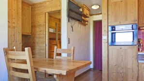 A wooden dining area with a table and chairs, a kitchen with a built-in oven, and a wooden wardrobe. - 10m from ski slopes, 1st floor, balcony, ski locker, 20m², Méribel-Mottaret (Méribel - Les Allues)