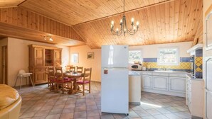 A spacious kitchen with wooden cabinets, a dining area with chairs, and a large refrigerator.