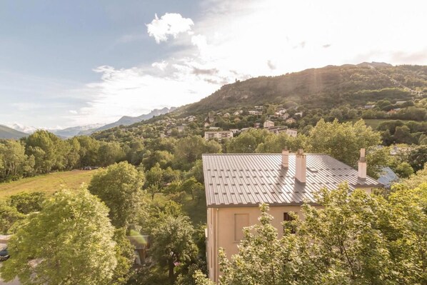 A building with a sloped roof, surrounded by lush greenery and a mountainous backdrop.
