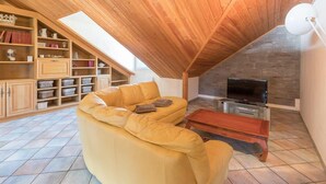 A cozy living room with a wooden ceiling, a yellow sofa, a TV, and a fireplace.
