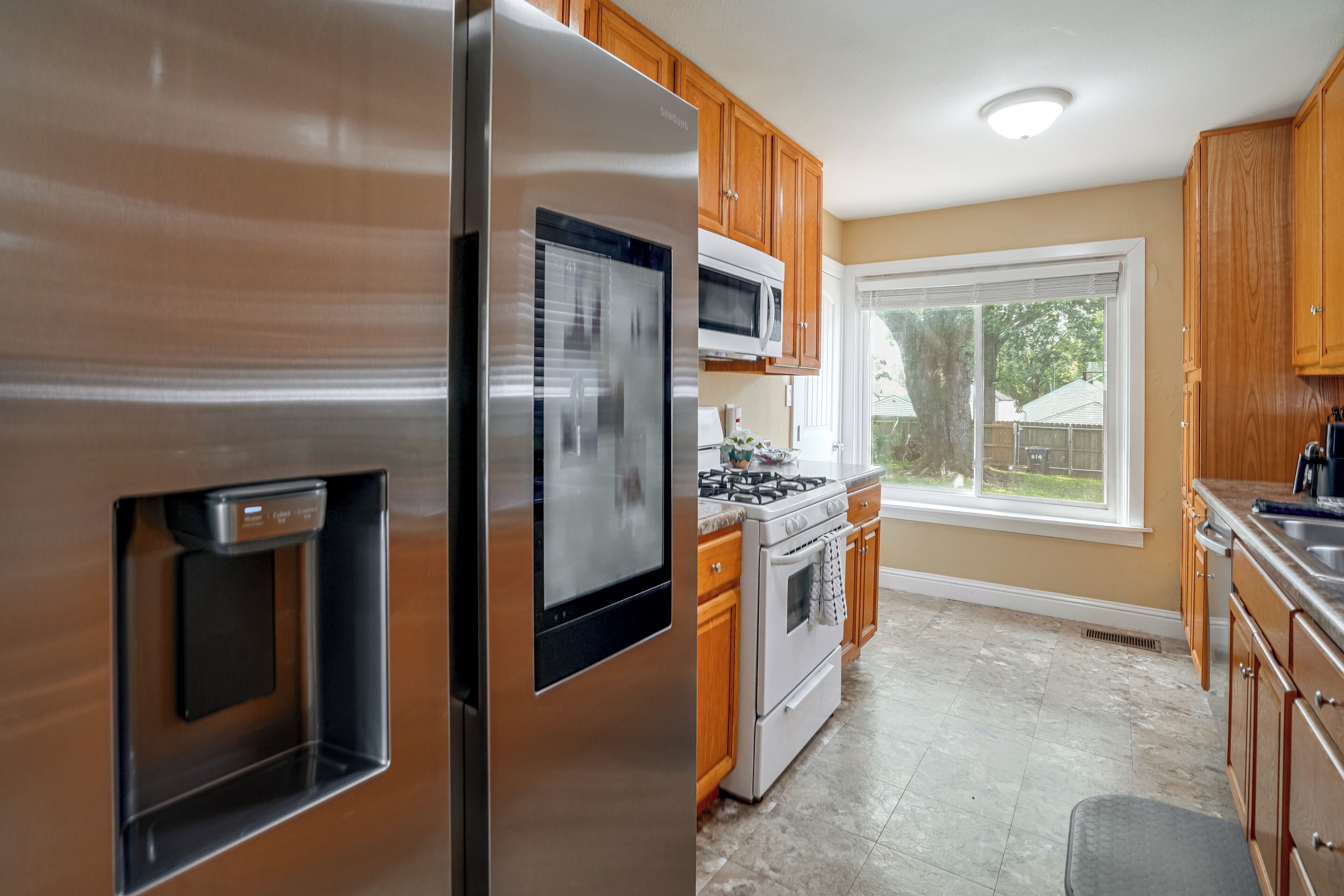 A kitchen with stainless steel appliances, wooden cabinets, a microwave, and a large window.