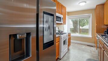 A kitchen with stainless steel appliances, wooden cabinets, a microwave, and a large window.