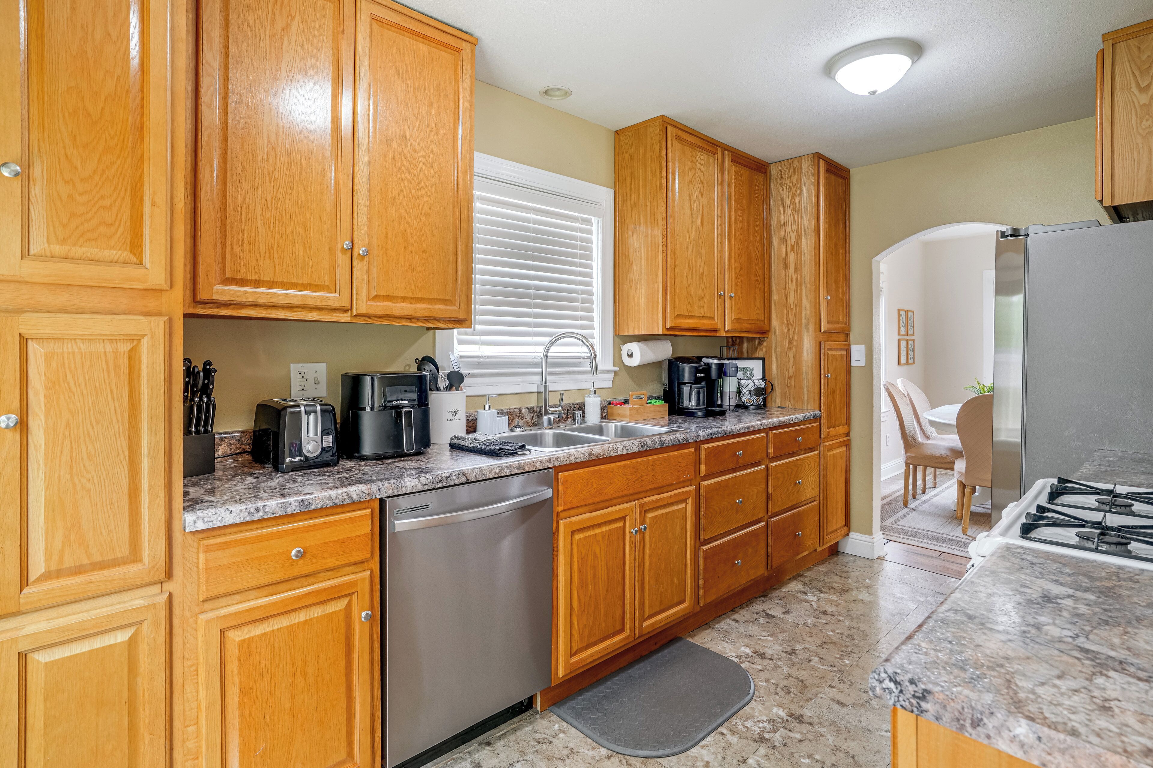 A kitchen with wooden cabinets, a stainless steel dishwasher, a granite countertop, and a gas stove.