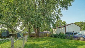 A fenced yard with a large tree, a shed, and a building with a garage. - Near Churchill Downs: Pet Friendly, Fenced Yard! (Louisville)