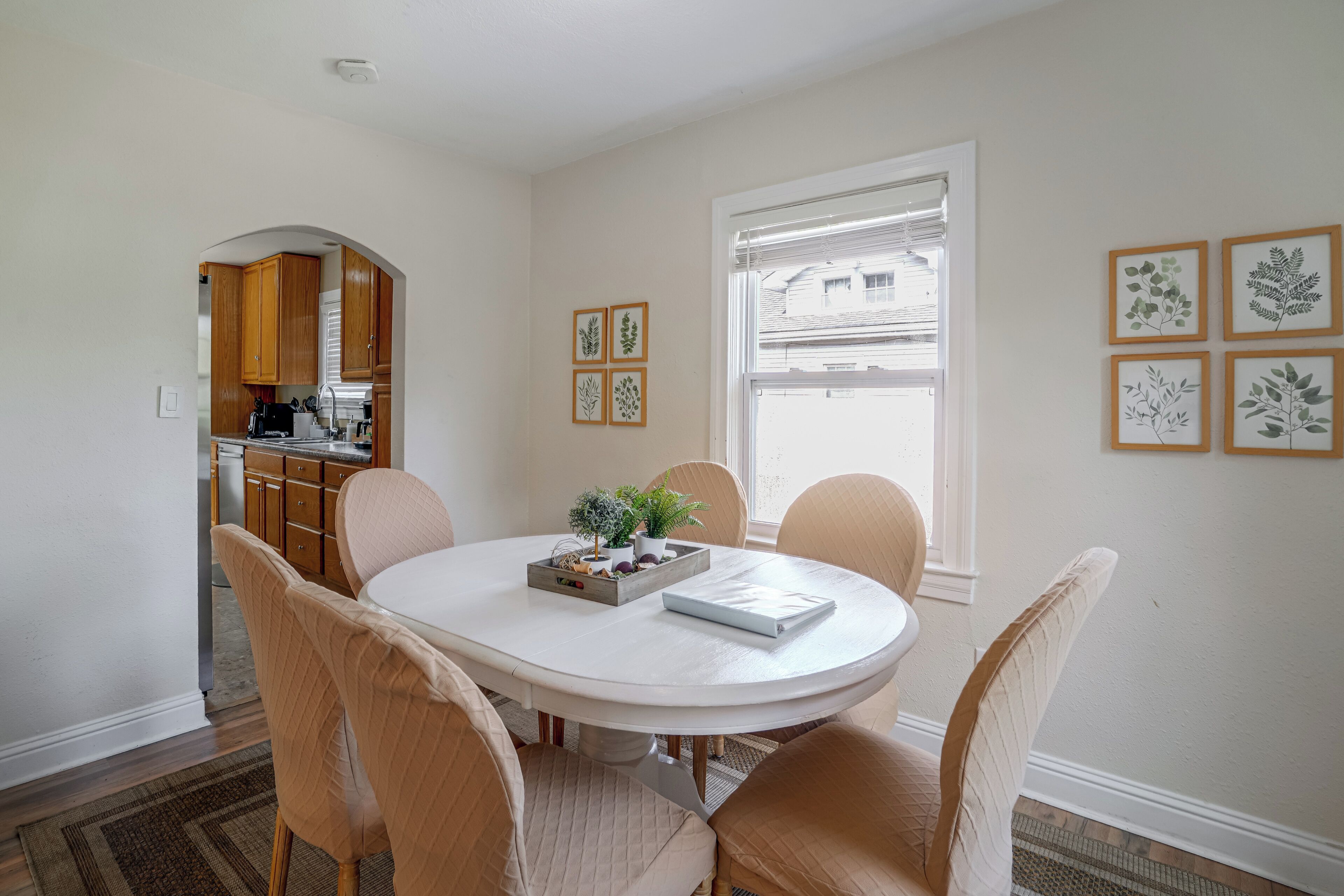 Un coin repas avec une table ronde, des chaises de couleur beige, une petite plante en pot et, au mur, des reproductions encadrées de dessins botaniques.