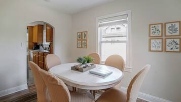 Un coin repas avec une table ronde, des chaises de couleur beige, une petite plante en pot et, au mur, des reproductions encadrées de dessins botaniques.