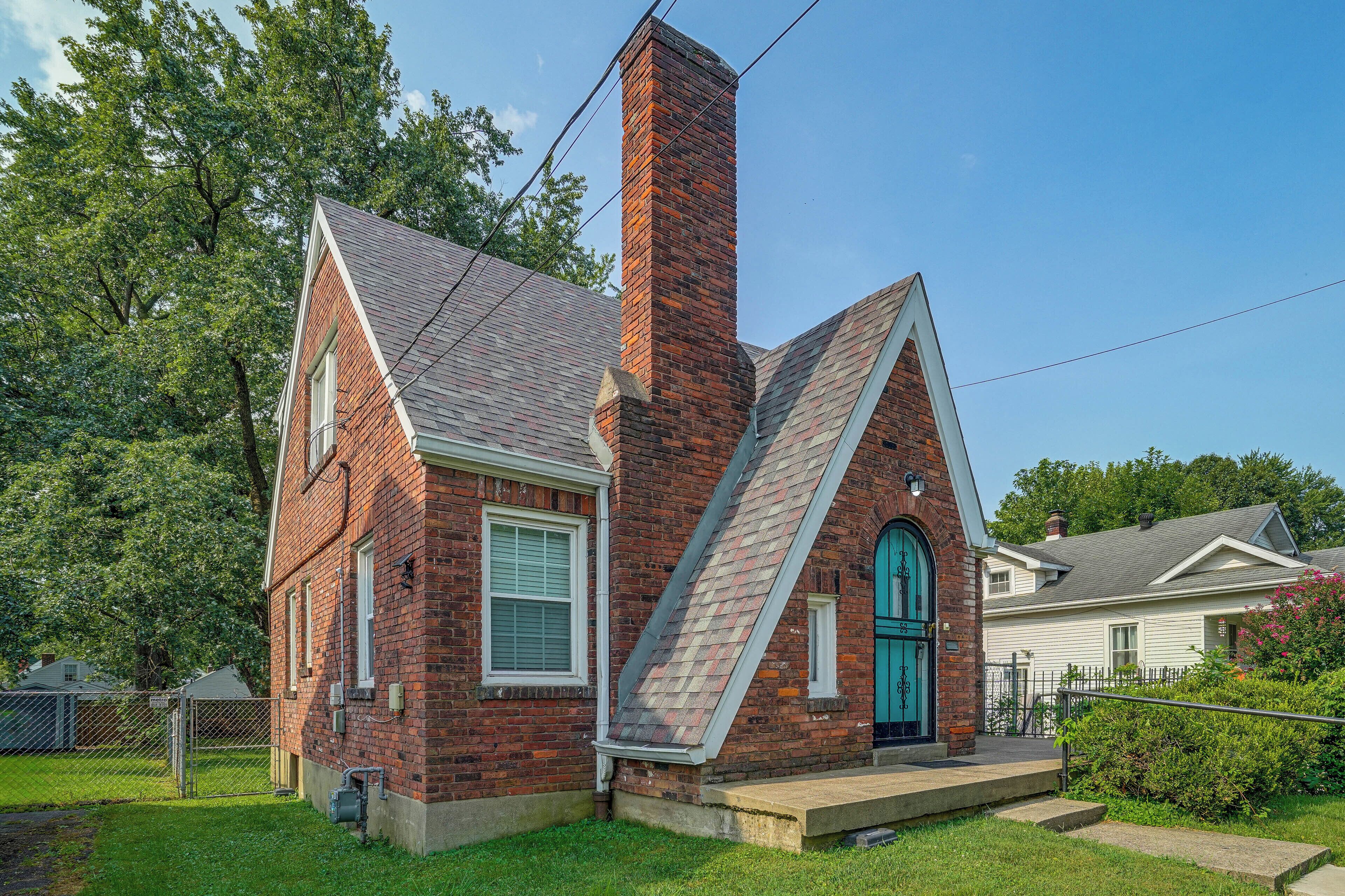 A brick house with a steeply pitched roof, a chimney, and a front door with a green door frame.