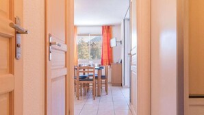 A corridor leading to a dining area with a table and chairs, a view of the outdoors, and a door on the left.