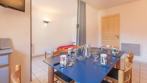 A dining area with a blue table set for four, including wine glasses, cups, and a pitcher. There is a TV mounted on the wall and a wooden door in the background.
