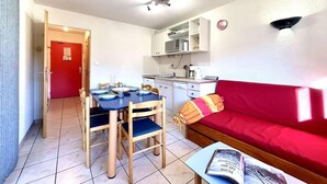 A compact living space with a dining table, chairs, a red sofa, a small coffee table, and a kitchenette.