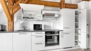Een moderne keuken met witte kastjes, een ingebouwde oven, een magnetron en een roestvrijstalen afzuigkap.