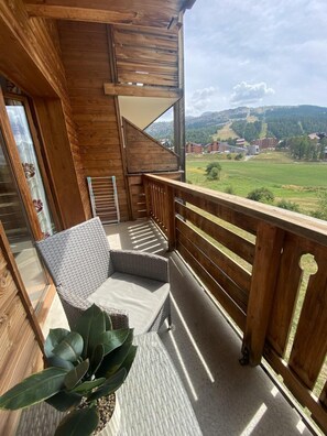 Un balcone in legno con una sedia in vimini e una pianta in vaso.