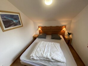 Un letto singolo con testiera in legno, due lampade ai comodini, un quadro appeso al muro e una piccola pianta su un tavolino di servizio.