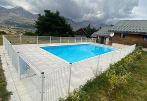 A rectangular swimming pool surrounded by a white fence, with a mountainous landscape in the background.
