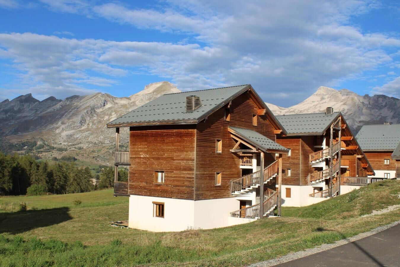 A wooden chalet with balconies, set against a mountainous backdrop.