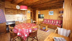 Een gezellig interieur van een chalet met een houten eettafel, stoelen, een bank, een televisie en een keukenhoek.