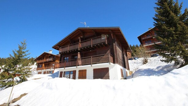 Een houten chalet met een balkon, omringd door sneeuw en bomen.