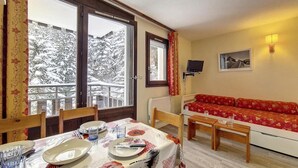 A dining area with a table set for two, a red sofa, and a view of snow-covered trees through large windows. - 2nd floor, balcony, tv, 24m², Les Menuires (Les Menuires)