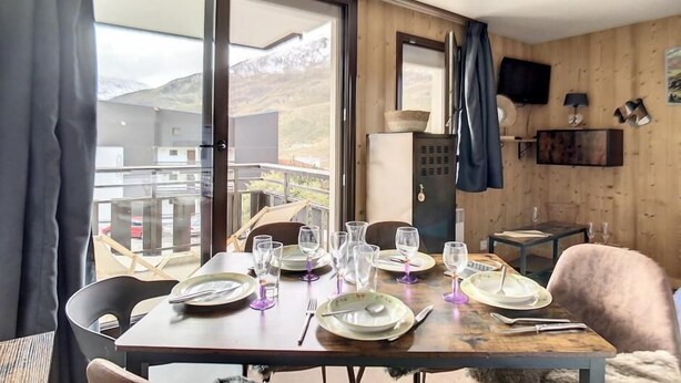 Ein Essbereich mit Tisch für vier Personen, einem an der Wand montierten Fernseher und Blick auf die Berge durch das Fenster.