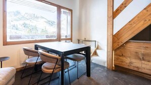 A room with a wooden table and chairs, large windows with a mountain view, and a sloped ceiling with exposed beams. - 5m from ski slopes, 9th floor, view panoramic, ski locker, 58m², Valmorel (Valmorel)