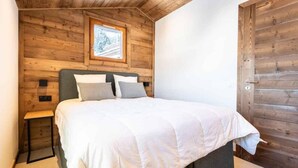 A bedroom with a wooden ceiling, a bed with white bedding, a nightstand, and a window with a view of trees. - 5m from ski slopes, 9th floor, view panoramic, ski locker, 58m², Valmorel (Valmorel)
