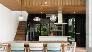 Un interior moderno con una escalera de madera, una zona de comedor con sillas tapizadas en azul claro e iluminación colgante.