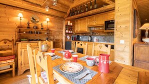 A rustic wooden interior with a dining table set for four, wooden cabinets, and a kitchen area with a stove and shelves. - 115m from ski slopes, view panoramic, balcony, ski locker, 87m², Valmorel (Valmorel)