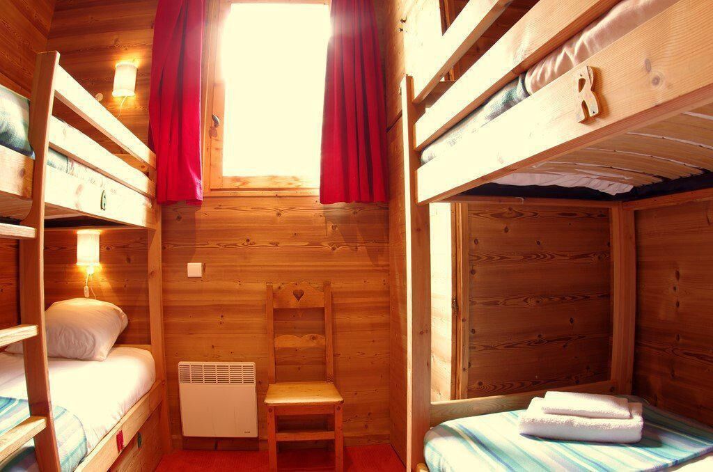 A wooden cabin room with bunk beds, a chair, a heater, and a window with curtains.