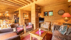 A cozy log cabin interior with a dining area, a living room with leather sofas and armchairs, a television, and a fireplace. - 115m from ski slopes, view panoramic, balcony, ski locker, 87m², Valmorel (Valmorel)