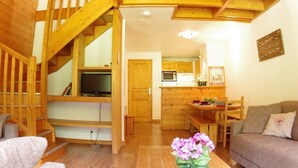 A wooden interior with a staircase, a living area with a sofa, a TV, and a kitchen area with a microwave. - 90m from shops, 5th floor, view mountain, balcony, tv, ski locker, 75m², Valmorel (Valmorel)