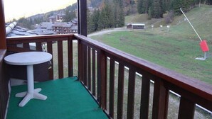 A wooden balcony with a green carpet, overlooking a mountainous landscape with buildings and a ski slope. - 90m from shops, 5th floor, view mountain, balcony, tv, ski locker, 75m², Valmorel (Valmorel)