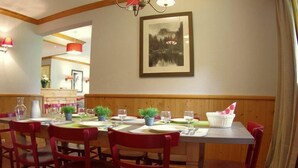 A dining area with wooden paneling, red chairs, a table set for four, and a framed picture on the wall.