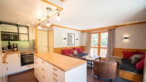 A cozy, well-lit room with a kitchen, a dining area, and a seating area with a sofa and a chair.
