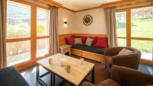 A cozy room with a wooden bench, a table with a teapot and cups, and a sofa with red cushions.