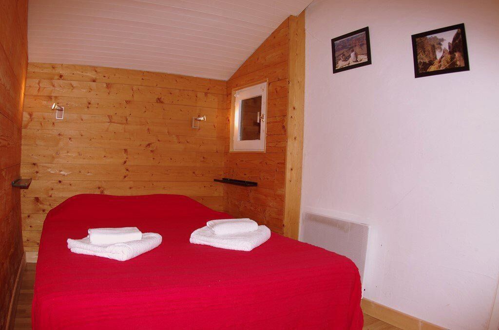 Une pièce aux murs lambrissés, contenant un lit, deux serviettes, une fenêtre et deux tableaux encadrés.