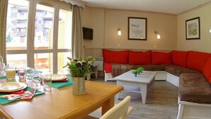 A living room with a sofa, a dining table set for two, and a TV mounted on the wall. - 250m from shops, 1st floor, balcony, ski locker, 55m², Valmorel (Valmorel)