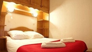 A neatly made bed with white linens and a red blanket, wooden headboard, and a wall-mounted light fixture. - 240m from ski slopes, 1st floor, view mountain, balcony, ski locker, 37m², Valmorel (Valmorel)