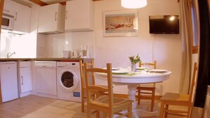 A compact kitchen with white appliances, a washing machine, and a dining area with wooden chairs and a table. - 240m from ski slopes, 1st floor, view mountain, balcony, ski locker, 37m², Valmorel (Valmorel)