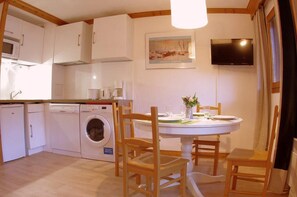 Une cuisine compacte avec des appareils électroménagers blancs, un lave-linge et un coin repas comprenant des chaises et une table en bois.