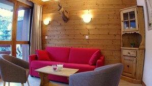 A cozy room with a red sofa, two armchairs, a wooden cabinet, and a deer head mounted on the wall. - 240m from ski slopes, 1st floor, view mountain, balcony, ski locker, 37m², Valmorel (Valmorel)
