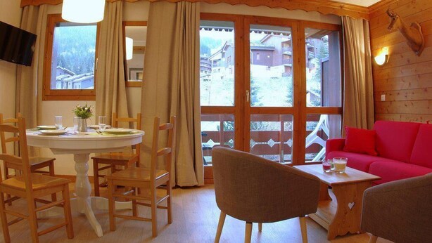 A cozy room with a dining table, chairs, a red sofa, and large windows offering a view of a snowy landscape. - 240m from ski slopes, 1st floor, view mountain, balcony, ski locker, 37m², Valmorel (Valmorel)