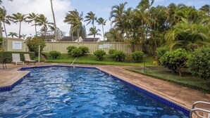 Ein Swimmingpool mit blauen Fliesen, umgeben von Palmen und einem Zaun.