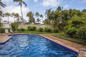 A swimming pool with blue tiles, surrounded by palm trees and a fence. - Beach Cozy North Shore Turtle Bay Condo (Kahuku)